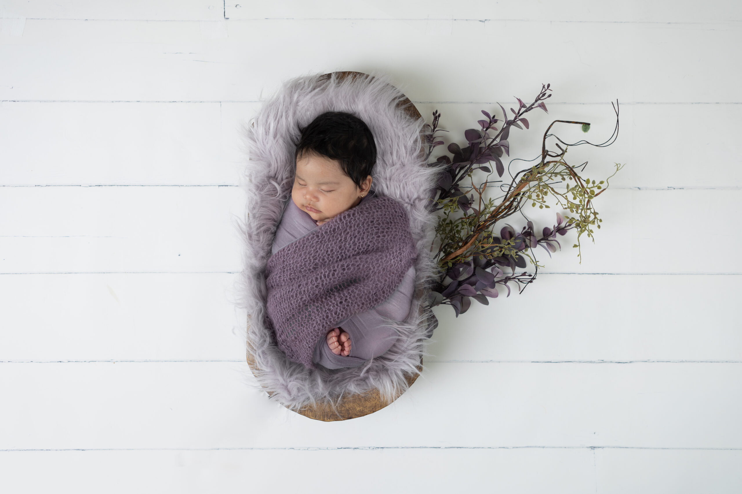 Newborn baby Girl in a two-tone purple wrap laying in a basket during a studio newborn session in Suwanee, Georgia