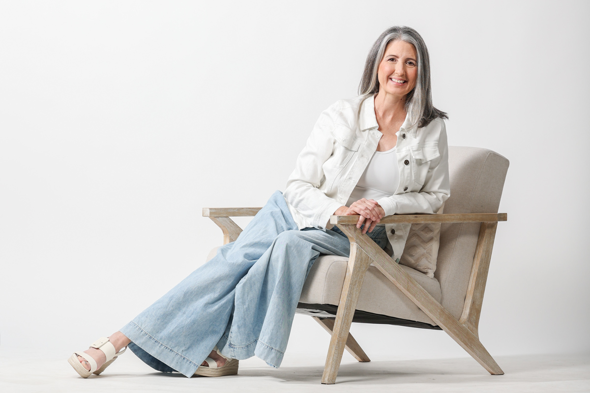 Alpharetta Studio Portrait of Woman in Lounge chair wearing jeans and a white jacket.